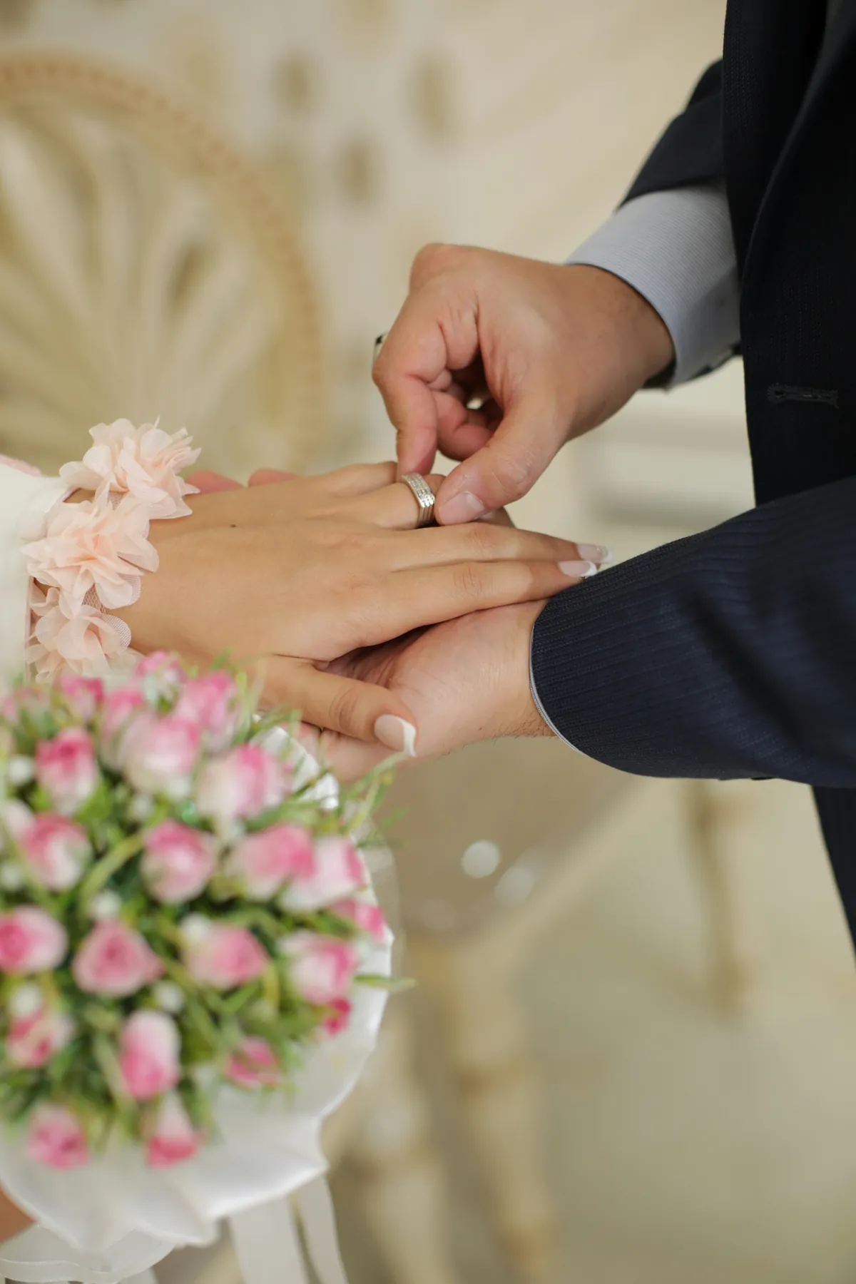 Brudgummen trär ringen på brudens finger under vigseln, med en rosa brudbukett i förgrunden